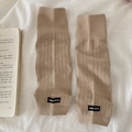 Scaldamuscoli in maglia a coste beige con etichetta del brand su sfondo libro - Taglia unica / Cachi