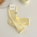 Hellgelbe Strick-Socken mit Lochmuster und schwarzer Schleifenbestickung in Wohnumgebung - Milchiges Gelb