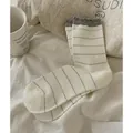 Japanese style cream mid-calf socks with grey stripes and ruffled cuffs on bedsheet - Cream