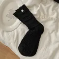 Calze nere a pieghe con trama ondulata e bottone bianco su sfondo minimalista - Nero