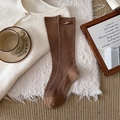Braune gerippte Baumwollsocken mit Lederetikett in einer warmen Lifestyle-Umgebung - Hellkaffee