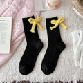Schwarze Strick-Wollsocken mit hellgelber Schleife auf weichem weißem Plüschteppich - Einheitsgröße / Schwarz