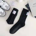 Schwarze Strickwollsocken mit hellblauem Bären-Aufnäher auf einem minimalistischen Tisch - Schwarz