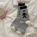 Calzini grigi in maglia con orsetto nero e fiocco bianco in un ambiente domestico relax - Grigio Medio