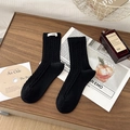 Classic black cable knit crew socks with minimalist white egg label on dark wood desk - One Size / Black