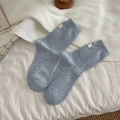 Blue-grey speckled knit crew sock with white logo patch on a cozy white blanket - One Size / Blue