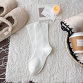 Minimalist white wool maternity socks shown on a cozy plush rug in a warm setting - White