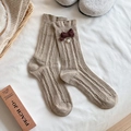 Calcetines de punto beige con lazo vintage y perla en un ambiente hogareño acogedor - Caqui