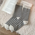 Schicke beige-schwarz gestreifte Wollsocken auf einem weichen weißen Plüschteppich - Cremeweiß mit schwarzen Streifen