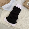 Black ribbed knit leg warmers with flared cuffs, shown in a cozy aesthetic lifestyle setting - Black