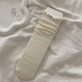 Creamy white frilly socks with bow jacquard pattern and ruffled edges in a cozy setting - Beige