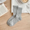 Chaussettes en tricot gris avec motifs ajourés et bords à volants sur bois - Taille unique / Gris foncé