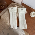 White ribbed knit leg warmers with metallic letter plaque on a wooden background - White