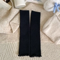 Black ribbed knit leg warmers with ruffled edges shown in a cozy winter setting - One Size / Black