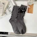 Dark gray knitted socks with black ribbon flower and ruffled cuffs on a minimal desk - One Size / Gray