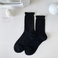 Black crew socks featuring vertical ribbed texture and delicate ruffle hem on white background - Black
