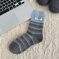 Blue and grey striped wool socks with a decorative logo tag on a soft white carpet - Medium Grey Stripe