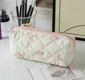 Close-up of quilted cream makeup bag with pink bow patterns and a zipper closure - White with Pink Bow