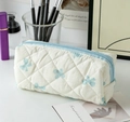 Detail view of a quilted cream makeup bag with light blue bows and zip closure - White Background Blue Bow