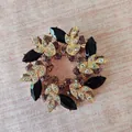 Detailed view of a round floral brooch featuring purple rhinestones and golden leaves - Purple Black Wreath Style