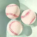 Three floating baseball-shaped bath toys with red stitching in light blue water - Bath Baseball Ball