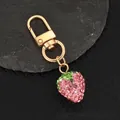 Close-up of a pink rhinestone strawberry keychain on a stone with gold metal clasp - Pink