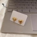 Detailed view of polished golden 3D heart stud earrings on a white display card - Gold Pair / Gold