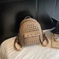 Beige faux leather backpack with silver studs and front zipper pocket on desk - Khaki