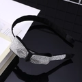 Dettaglio del cerchietto nero con fiocco e strass scintillanti su superficie a specchio - Cerchietto con fiocco in strass bianchi
