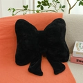 Soft black faux rabbit fur pillow in a bow shape with ribbons on a knitted blanket - Black