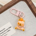 Cute orange cartoon bear keychain with pink lobster clasp on decorative textile background - Persimmon Bib