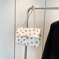 Close-up of white corduroy shoulder bag with strawberry print and gold chain strap - White