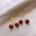 Detailed close-up of golden bow cherry earrings on elegant purple silk fabric - Bowknot Cherry Stud Earrings (Real Gold Plated)