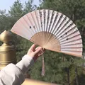 Pink silk folding fan with butterfly patterns and a matching tassel held outdoors - Pink Butterfly Floral Style (Fan 14)