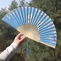 Blue folding fan with white crane motifs, bamboo ribs, and silk tassel in hand - Blue Crane & Plum Blossom Style (Smile Fan 86)