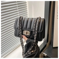 Detail view of black quilted crossbody bag featuring silver metal chain and twist lock clasp - Black