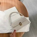 Beige faux leather shoulder bag with crocodile texture and gold clasp on a table - White