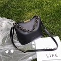 Chic black leather bucket bag with gold chain and adjustable strap on a green grass setting - Black