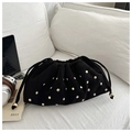Detalle de bolso nube de ante negro con remaches dorados sobre un sofá blanco texturizado - Negro
