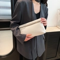 White woven envelope crossbody bag with gold buckle on a gray blazer commute style - White