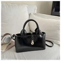 Detalle de bolso bandolera negro brillante con colgante dorado en un sofá beige - Negro