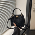 Black leopard print crossbody bag with gold buckle and top handle in modern setting - Black