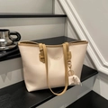 Minimalist beige leather tote bag with brown handles and elephant charm in indoor setting - White