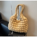 Detalle del bolso tote acolchado beige con textura de burbujas sobre un libro negro - Caqui