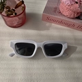 Detalle de gafas de sol rectangulares blancas con montura gruesa y lentes oscuras sobre mesa - Blanco