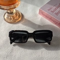 Detail of square black resin sunglasses on a white textured table with sunlight shadows - Black