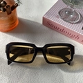 Close-up of rectangular black frames with amber lenses next to a cinnamon roll and book - Black and Yellow