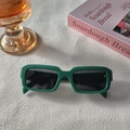Détail de lunettes de soleil carrées vert foncé sur un support décoratif moderne - Vert