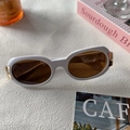 Close-up of white oval frame sunglasses with brown lenses and gold metal accents - White