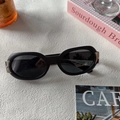 Unisex oval black resin sunglasses with silver metal hinges on a lifestyle background - Matte Black